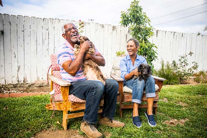 Senior couple holds dogs in yard.