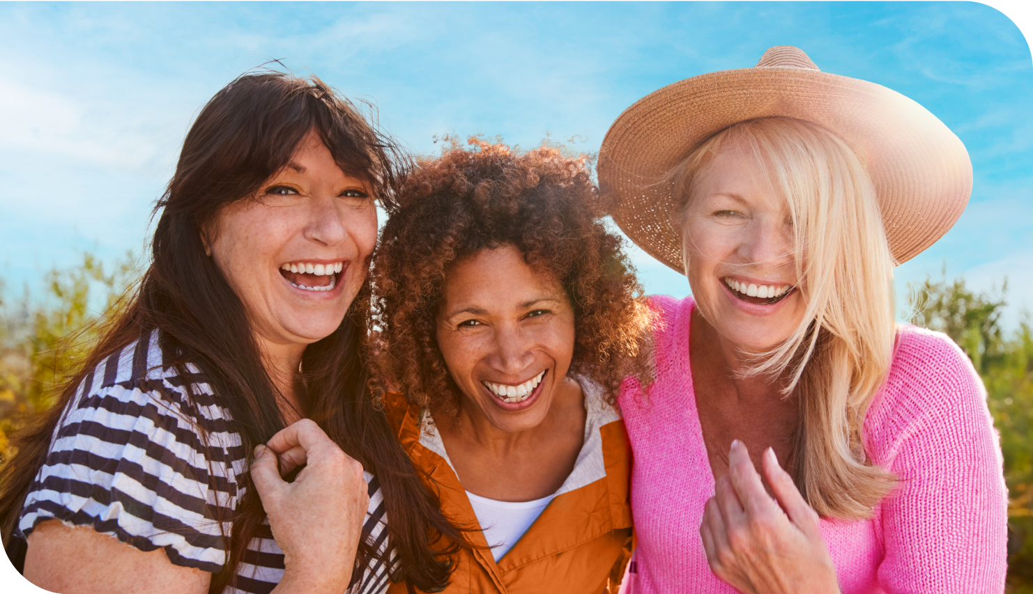 group of three middle aged friends laughing outdoors on a sunny day.
