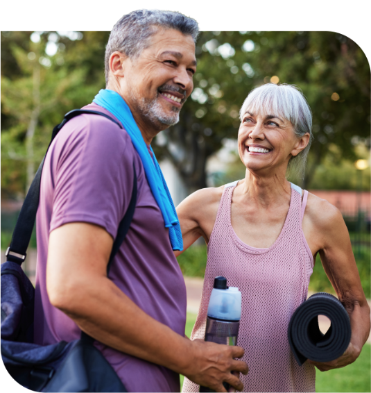 A smiling couple outdoors carrying a yoga mat and water bottle after a workout