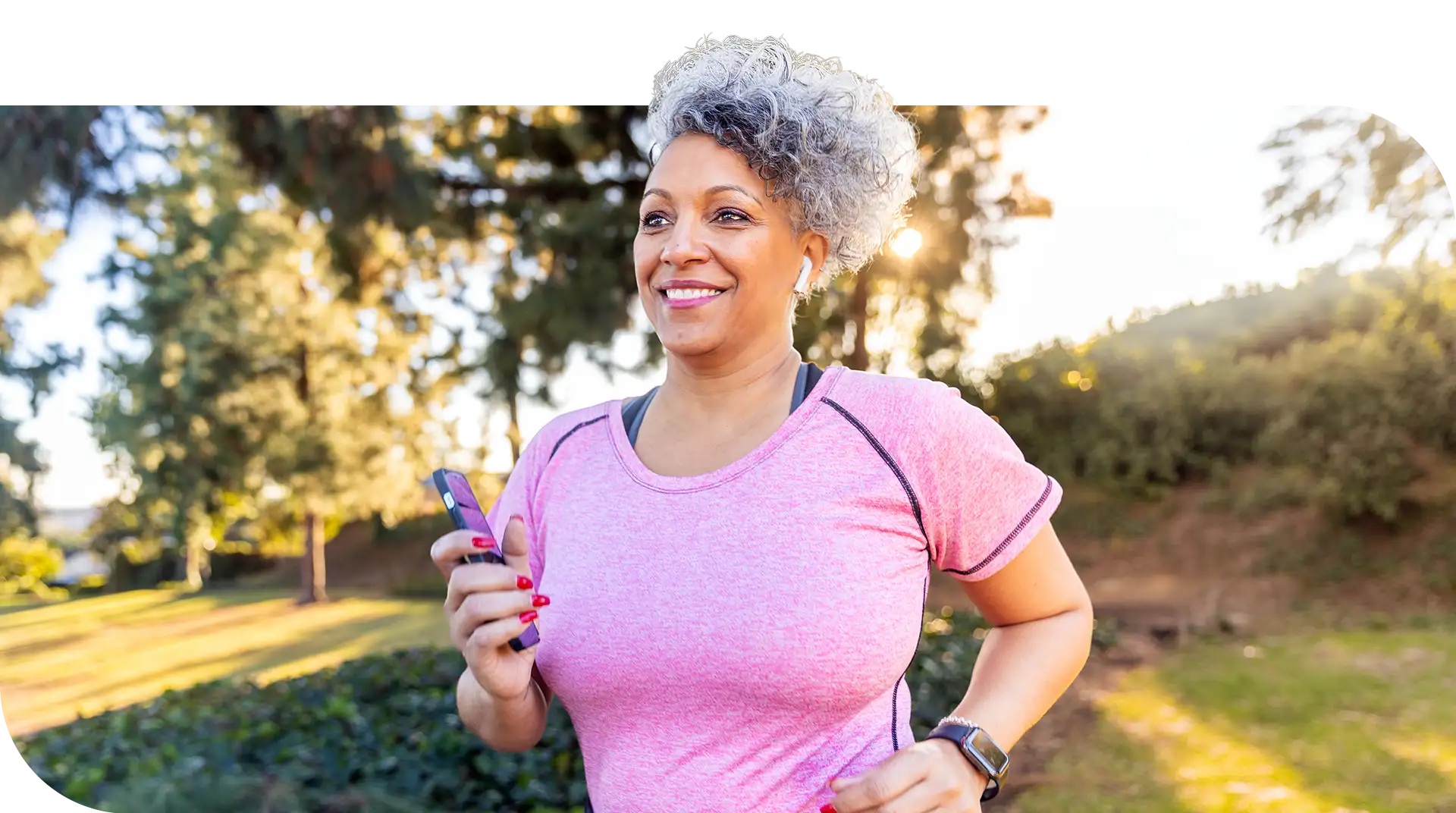 Smiling older woman jogging outdoors while holding her phone